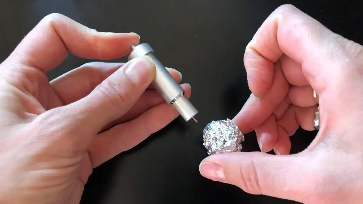 Cricut premium fine point blade being stabbed into a aluminum foil ball to clean the blade